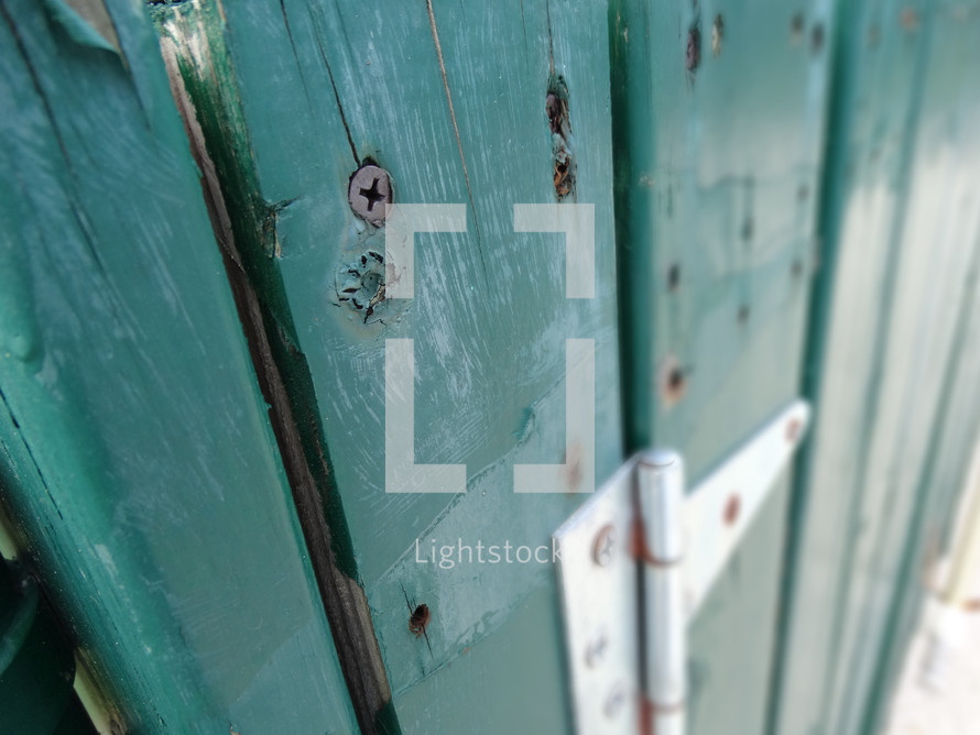 Close up of screws in green wooden fence with silver hinge