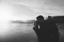 man taking a picture with a camera outdoors by a lake 
