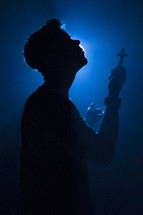 a man holding a cross illuminated in darkness 