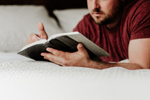 man lying on a bed reading a Bible 