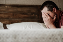 a man covering his face kneeling over a bed 