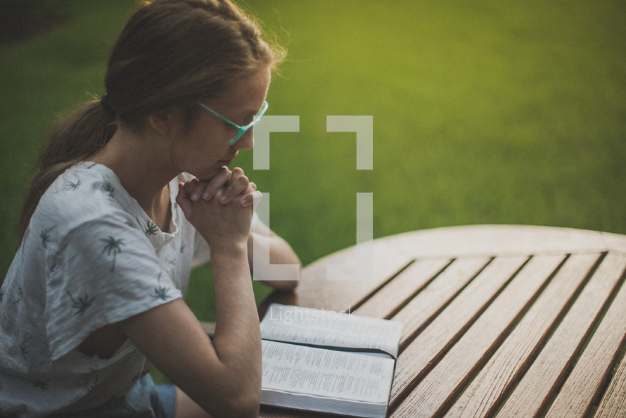 a young woman reading and praying over a Bible in her backyard 