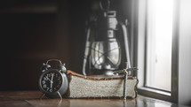 alarm clock, Bible, cross, and oil lamp in a window 