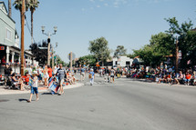 people sitting along sidewalks to watch a parade 