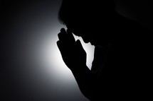 Silhouette of an Asian woman praying
