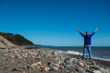 man standing on a shore with raised hands 