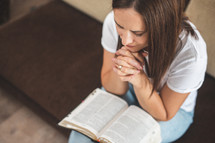 a woman sitting on a couch praying over a Bible 