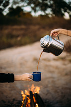 pouring coffee from a coffee pot into a mug over a campfire 