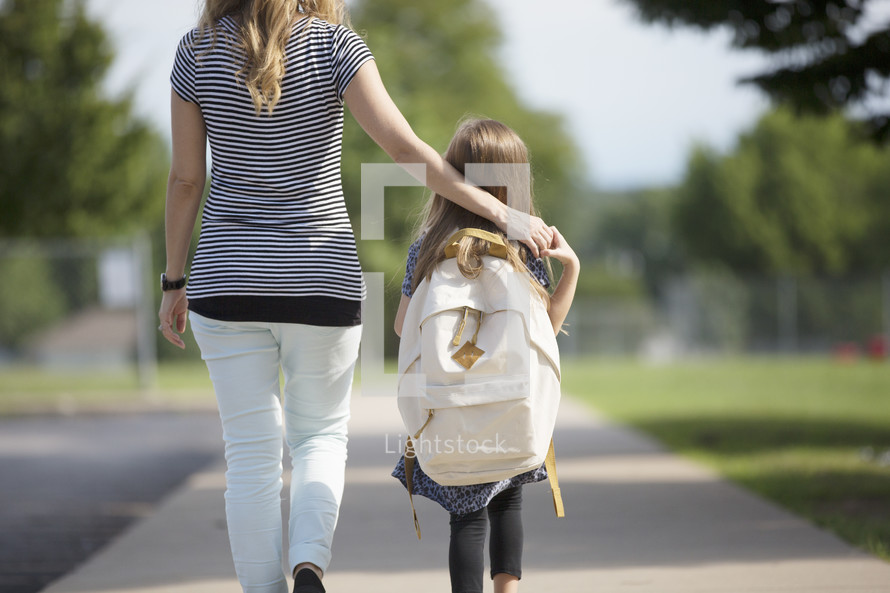 a young girl holding hands with mom while walking to school.