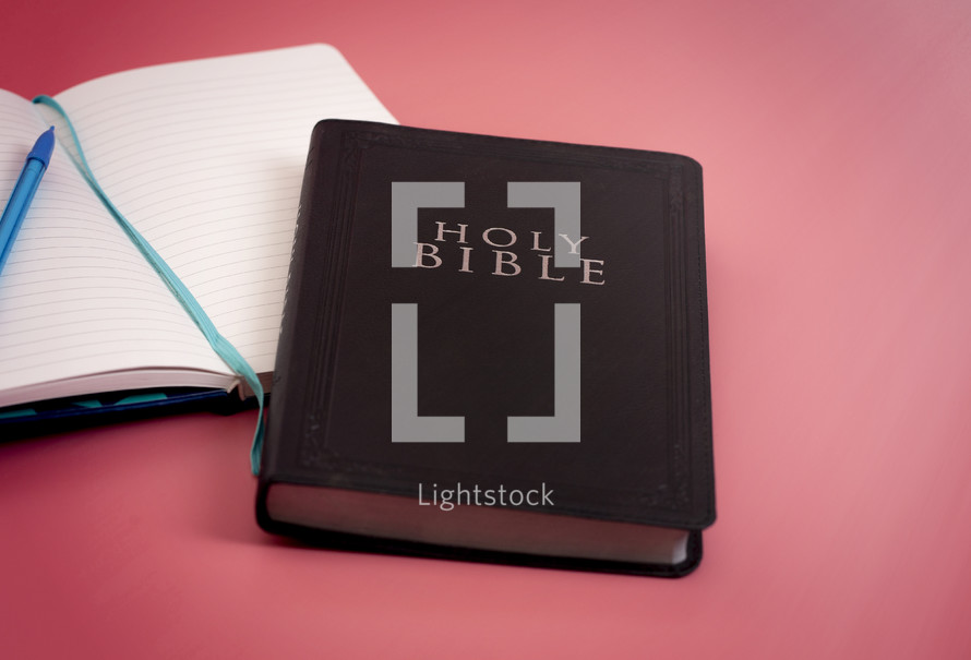 A Holy Bible with a Notebook to Study on a Bright Pink Background