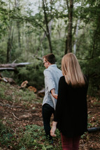 a couple walking holding hands in the woods 