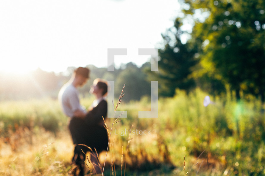 a couple standing in a field of tall grass in sunlight 