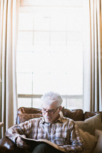 elderly man sitting on a couch reading a Bible