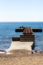 Two fisherman attempt to catch fish at the end of a pier on Old Town Beach in Budva, Montenegro