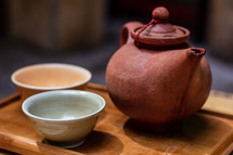 Clay oriental teapot and ceramic cup on a wooden tray