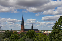 Profile of Uppsala Cathedral in Sweden under a blue sky with fluffy white clouds, green trees in the foreground
