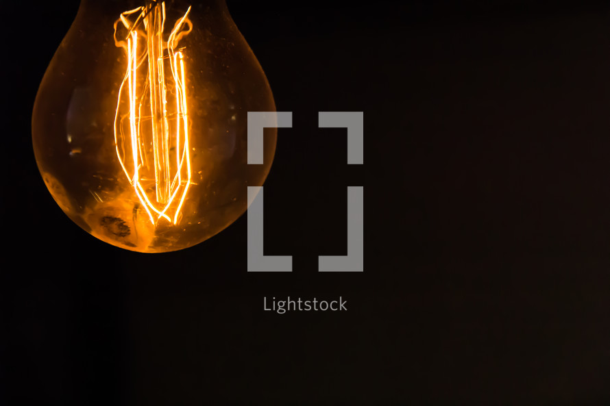 A naked retro light bulb in top left corner of the frame on a black background