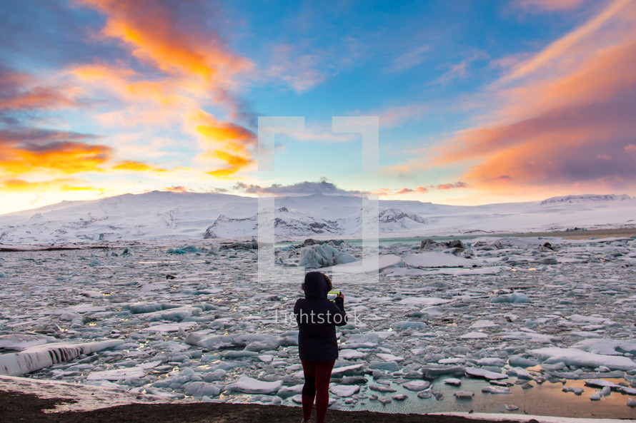 A woman in silhouette is phototraphing Glacier Lagoon (Jokulsarlon) at sunset with her mobile phone on the south coast of Iceland. It contains thousands of icebergs from the Breidamerkurjokull Glacier.