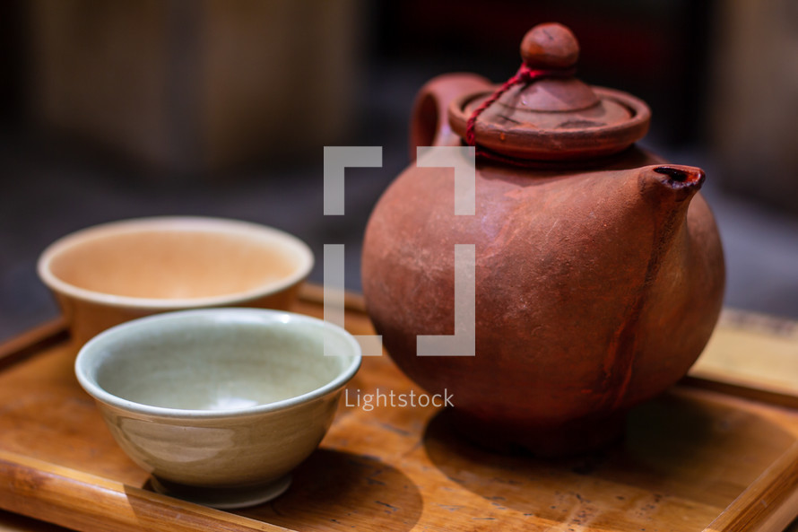 Clay oriental teapot and ceramic cup on a wooden tray