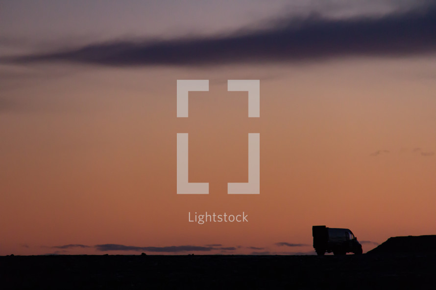 Camper van parked on a rocky landscape in silhouette against a colorfuly sky at sunset