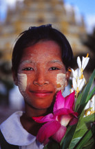 Burmese woman with painted face and tropical flowers outside a Buddhist temple