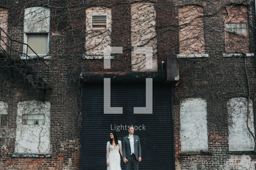 a bride and groom in front of a brick warehouse building 