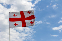 Flag of the Republic of Georgia waves in a strong breeze against a blue sky with white clouds