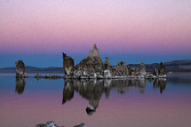 rock formation jutting out of still water at sunset 