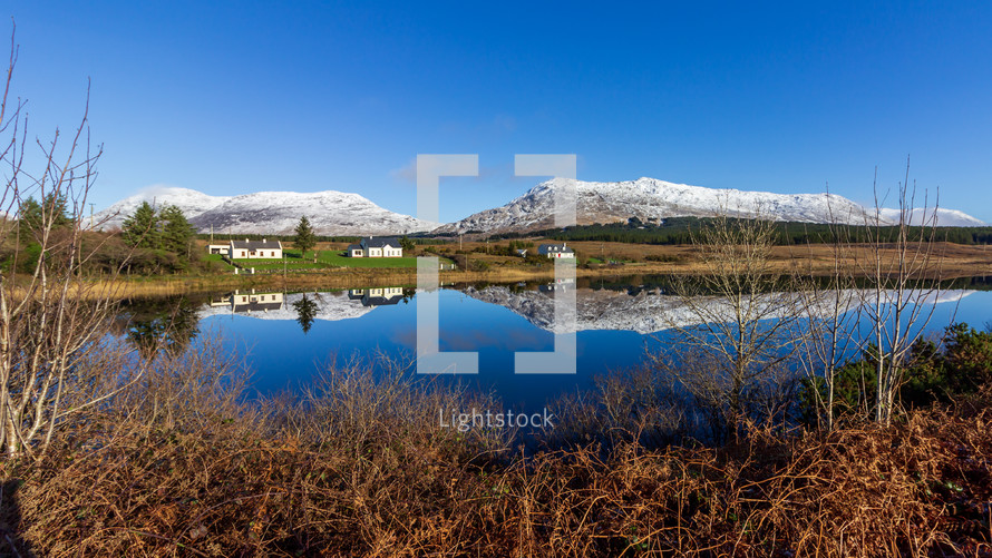 A lake in Connemara, Galway County, Ireland reflects houses, a mountain and sky on a sunny day