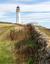 Rock wall leading to the Mull of Galloway lighthouse in Dumfries and Galloway, Scotland, United Kingdom under a blue sky with white clouds