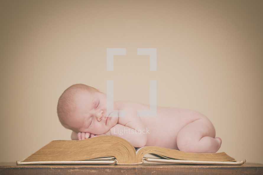 a newborn baby sleeping on a Bible 