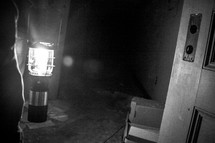 man carrying a glowing lantern into a dark abandoned room 