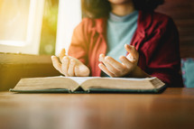 a woman sitting at a table praying over an open Bible 