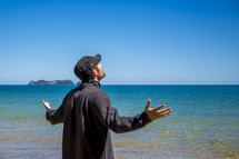 man standing on a beach with outstretch arms looking to God 