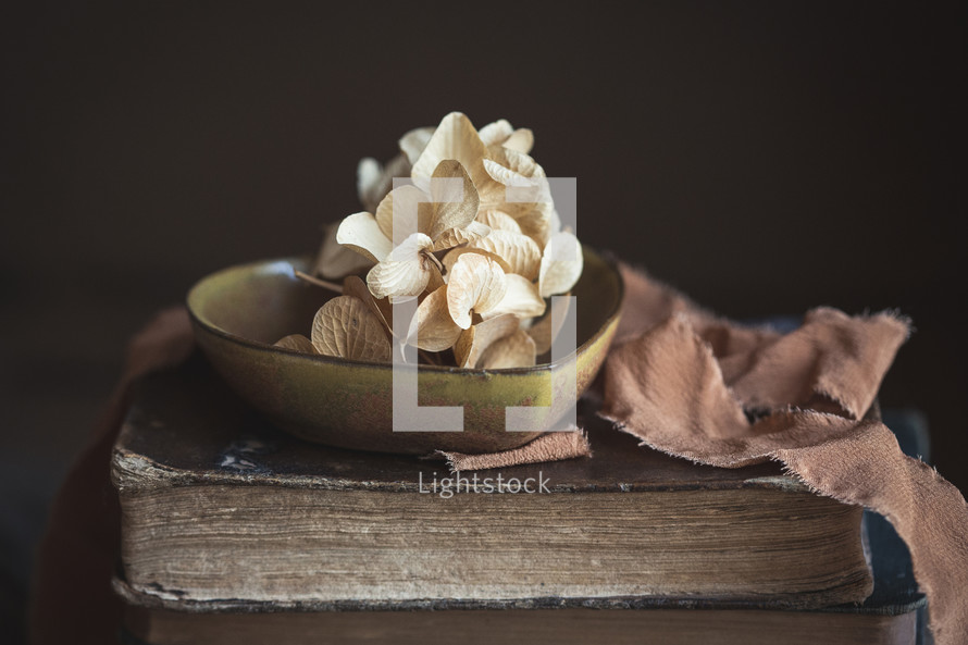 Tan flowers in a small heart dish on top of a Bible with strip of fabric