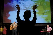 a woman with raised hands and worship leaders leading a congregation in song 