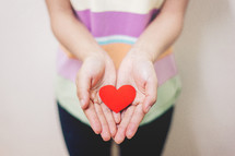 cupped hands holding a paper heart 