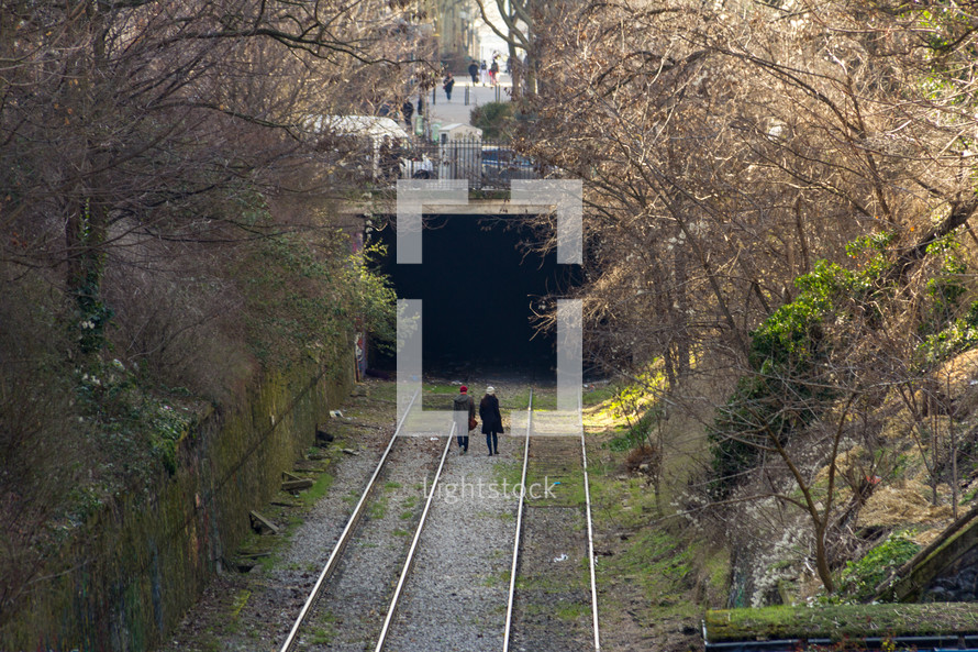 couple walks on train tracks towards a tunnel 