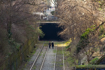 couple walks on train tracks towards a tunnel 
