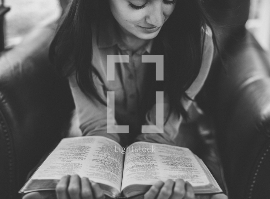 A young woman siting in a chair reading the Bible