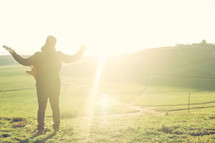 man with raised hands standing outdoors under intense sunlight 