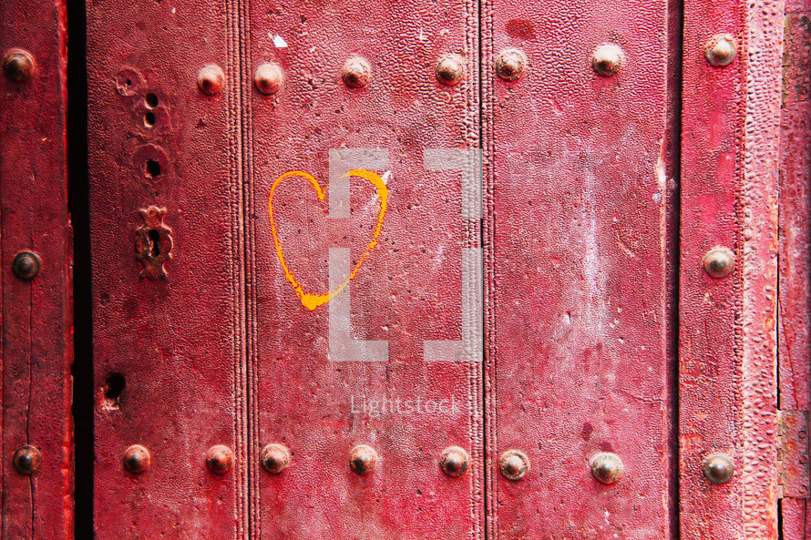 a yellow color heart painted onto a an old red door