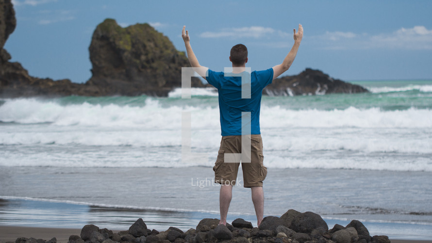 man standing on a beach with raised arms 