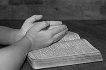 praying hands on the pages of a Bible 