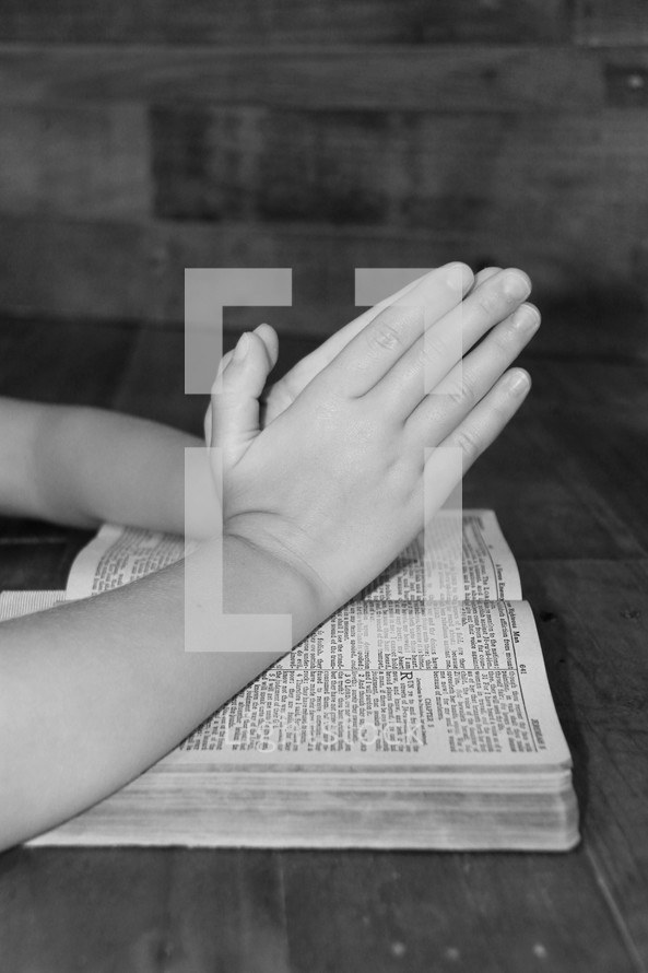 praying hands on the pages of a Bible 