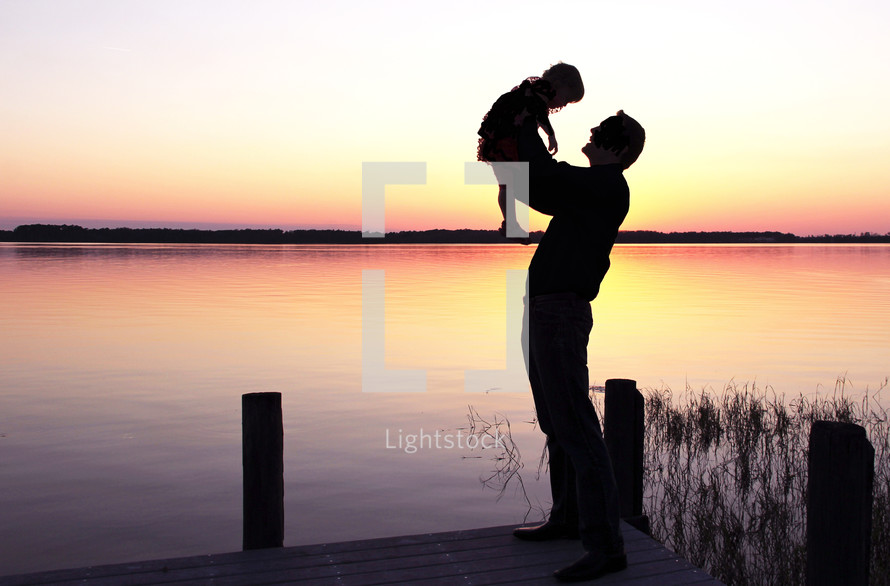 silhouette of a father holding up his son in front of a lake