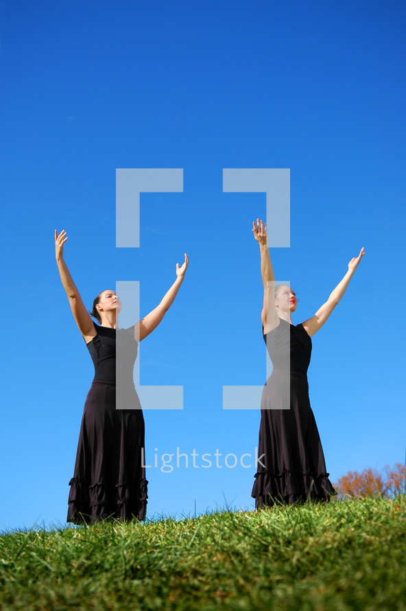 Two woman, on a hillside, with their arms raised