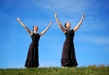Women with arms raised in praise in a field of grass.