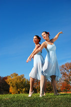 Two women dancers, in a field, with autumn foliage on trees in the background