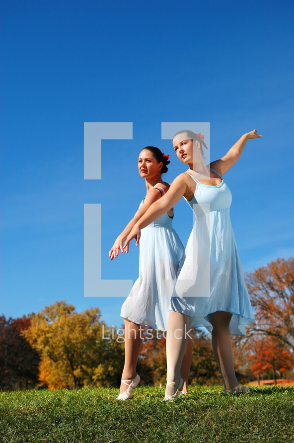 Two women dancers, in a field, with autumn foliage on trees in the background